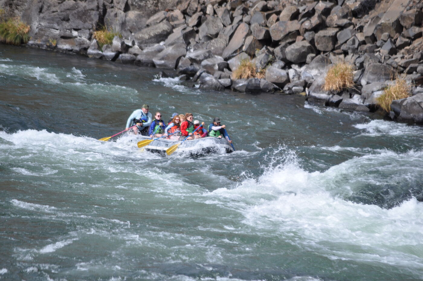 A raft full of paddlers in life jackets punching through whitewater on the Deschutes River